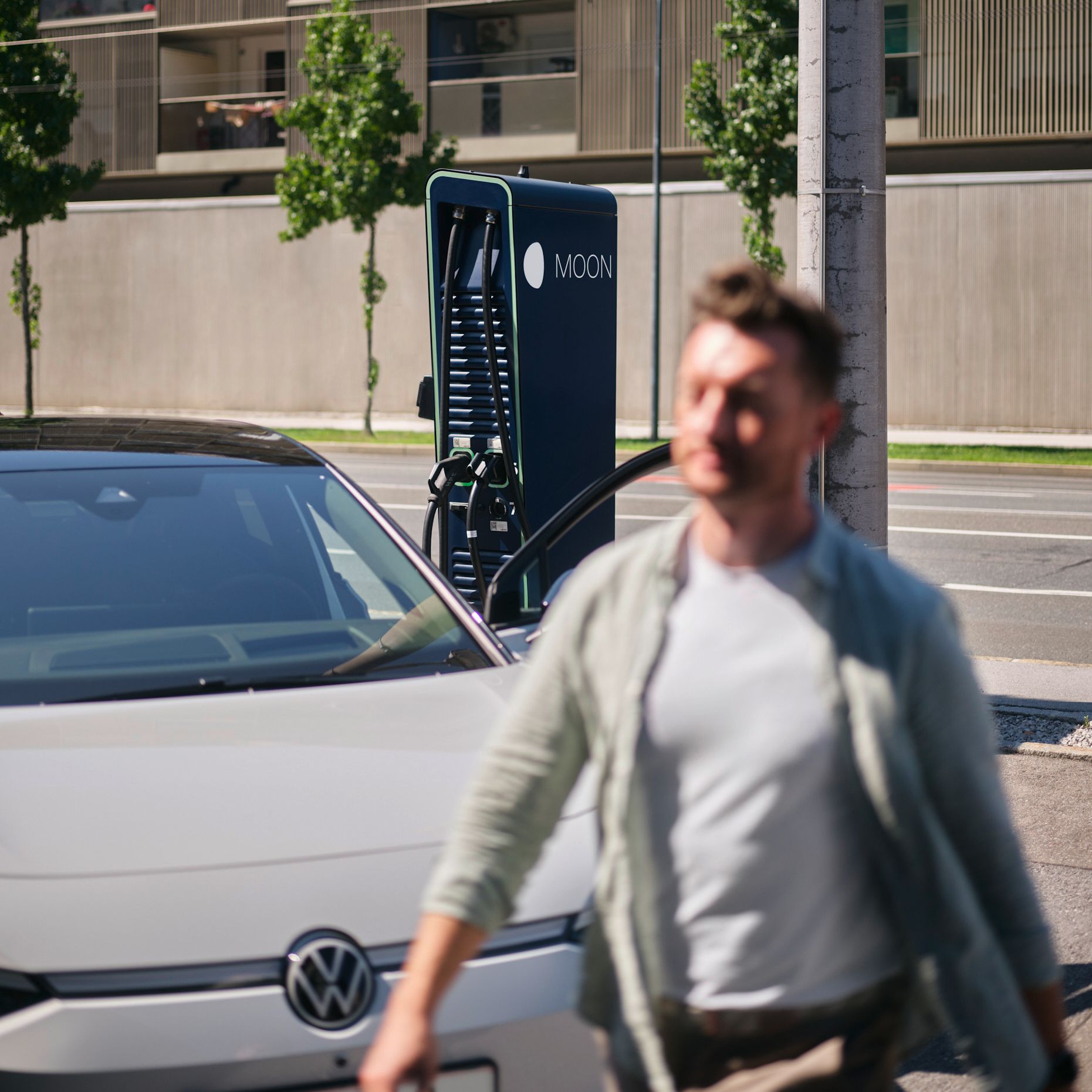 Man walks in front of an electric car in front of a fast charging station