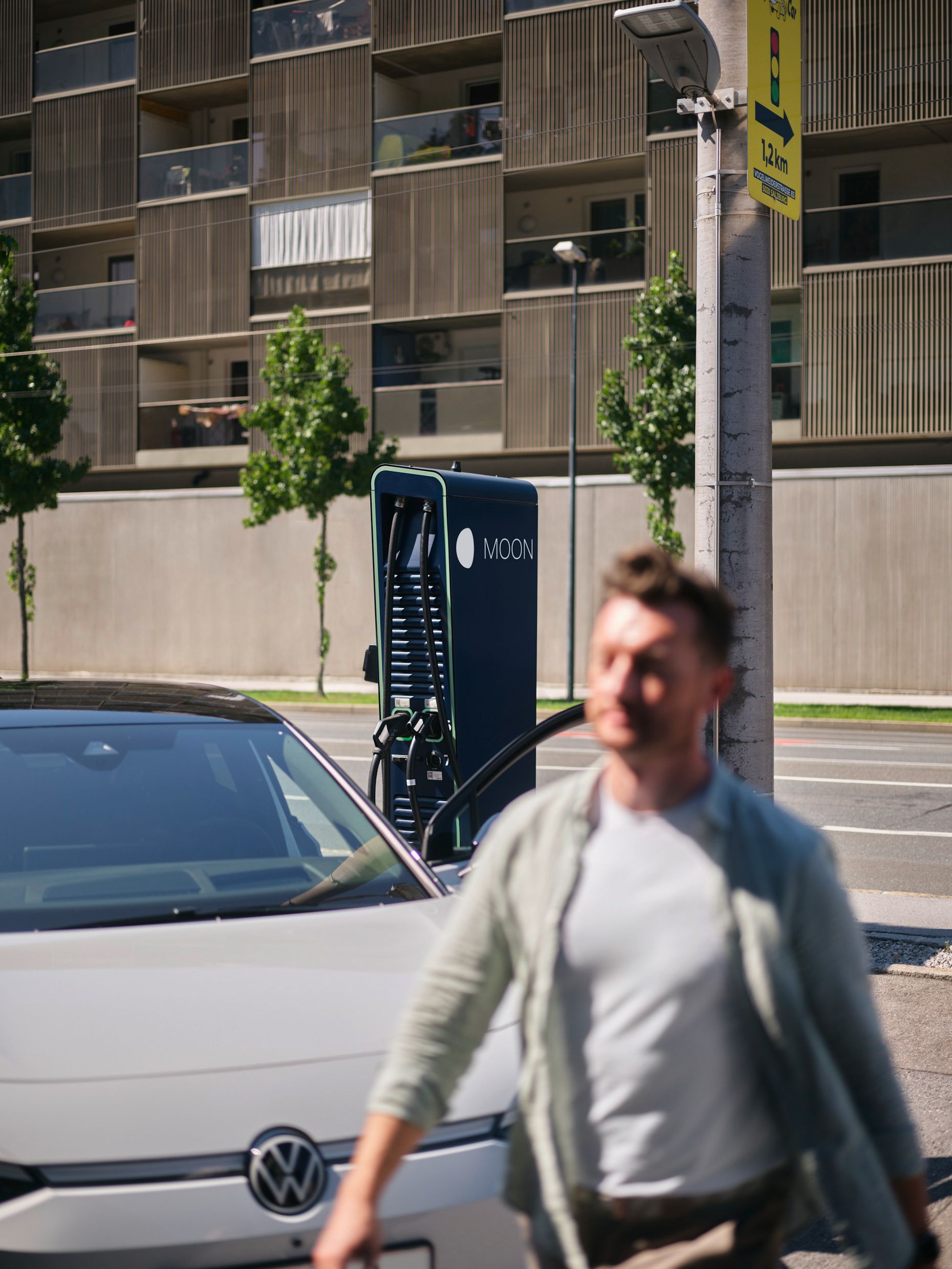 Man walks in front of an electric car in front of a fast charging station